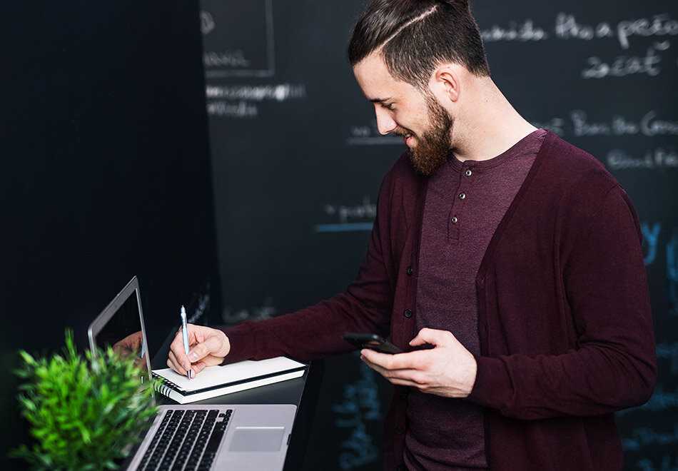 A man writing on a piece of paper while looking at a laptop