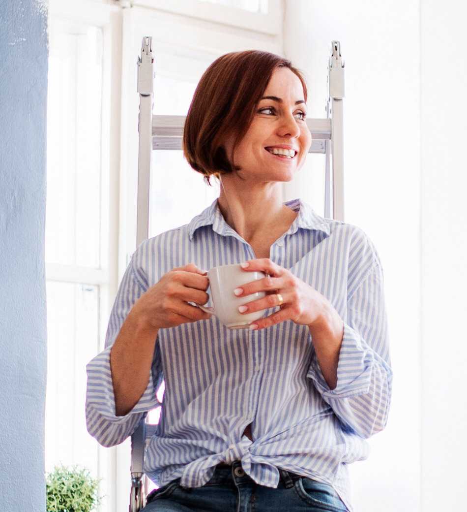 A woman standing on a ladder and having a break, drinking a hot beverage