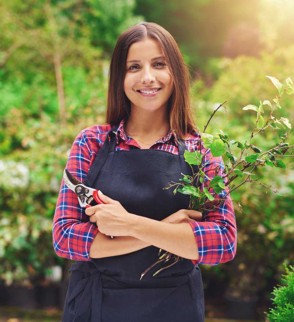 A female gardener holding a cutting tool in one hand and cut branches in her other hand